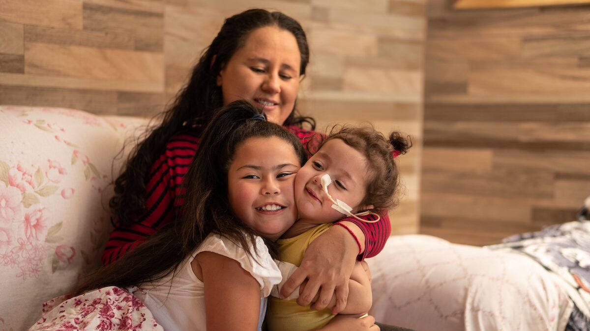 Mother and sister embracing child with disability in simple living room